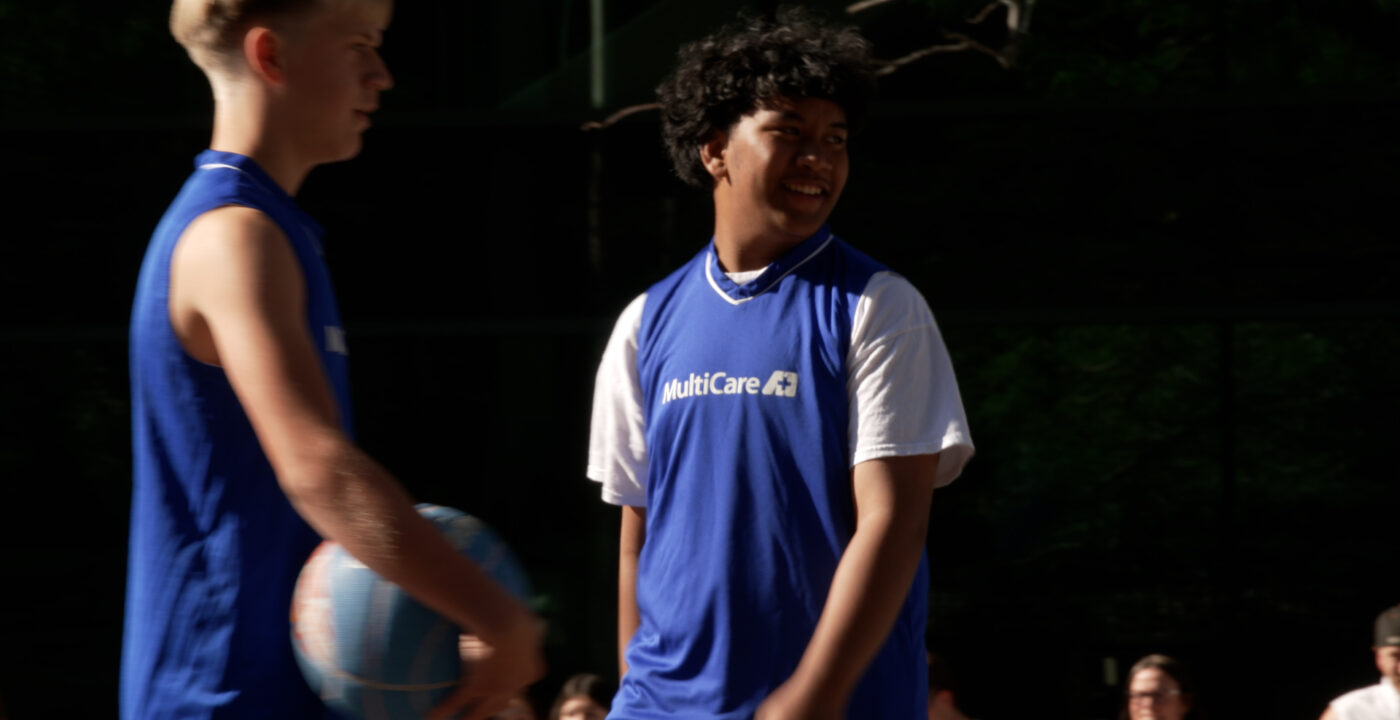 Two boys playing basketball wearing blue tank tops with MultiCare printed on the front.