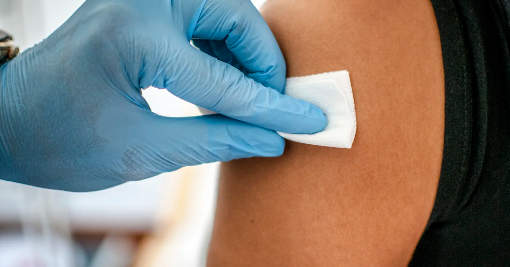 Health care provider’s gloved hand using an antiseptic wipe on a patient’s skin