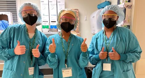 Three M.A.S.H. camp participants dressed in surgical scrubs, masks and protective eye gear.