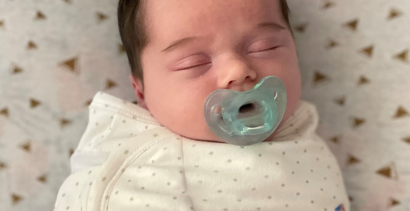 Infant laying on back, swaddled with pacifier in mouth.