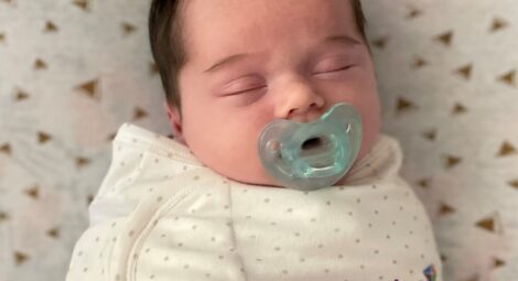 Infant laying on back, swaddled with pacifier in mouth.