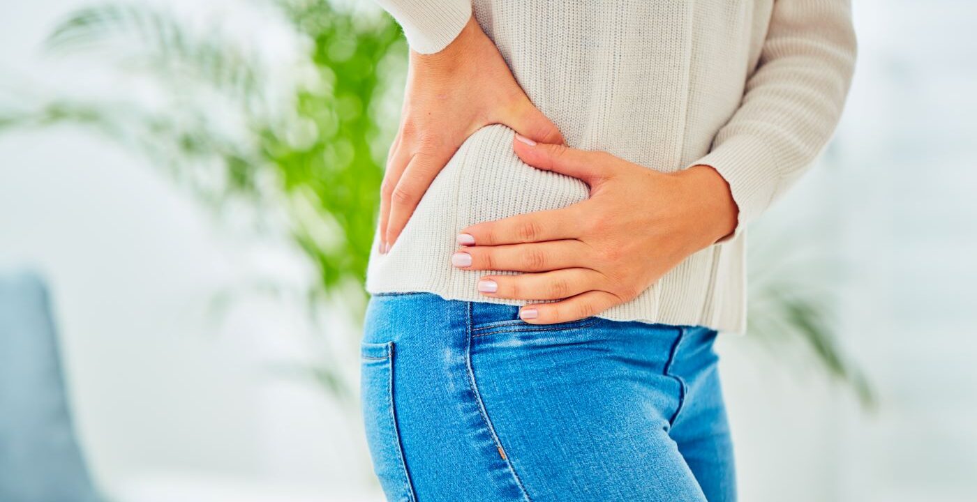 Torso of woman in sweater and jeans gripping right hip.
