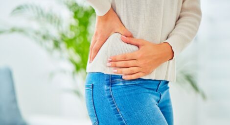 Torso of woman in sweater and jeans gripping right hip.