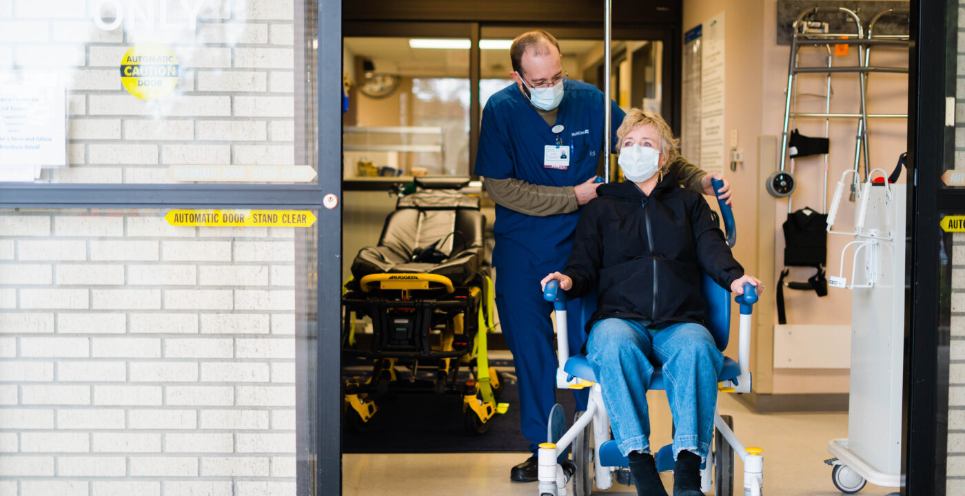MultiCare provider guiding patient in a wheelchair out of the emergency department