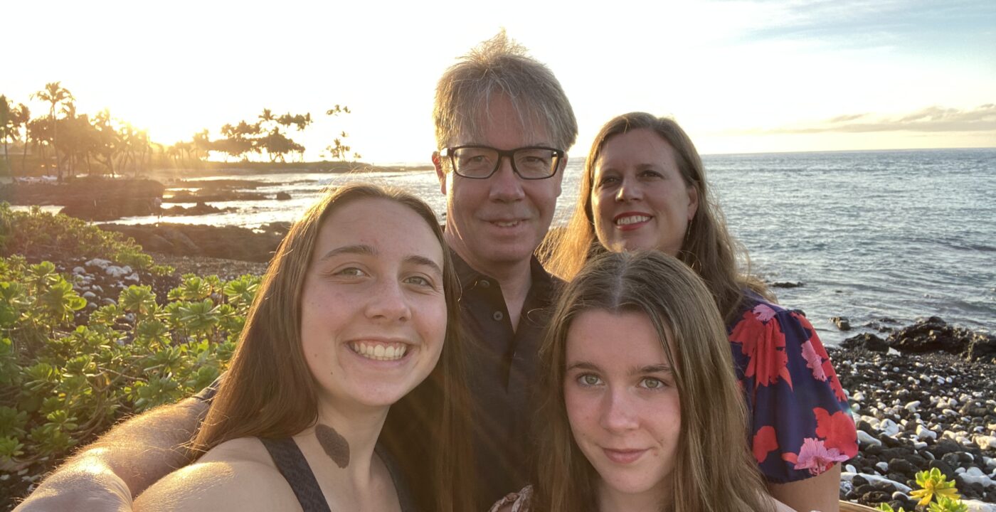 Dad, mom and two daughters smile for a selfie on the beach