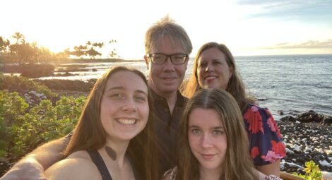 Dad, mom and two daughters smile for a selfie on the beach