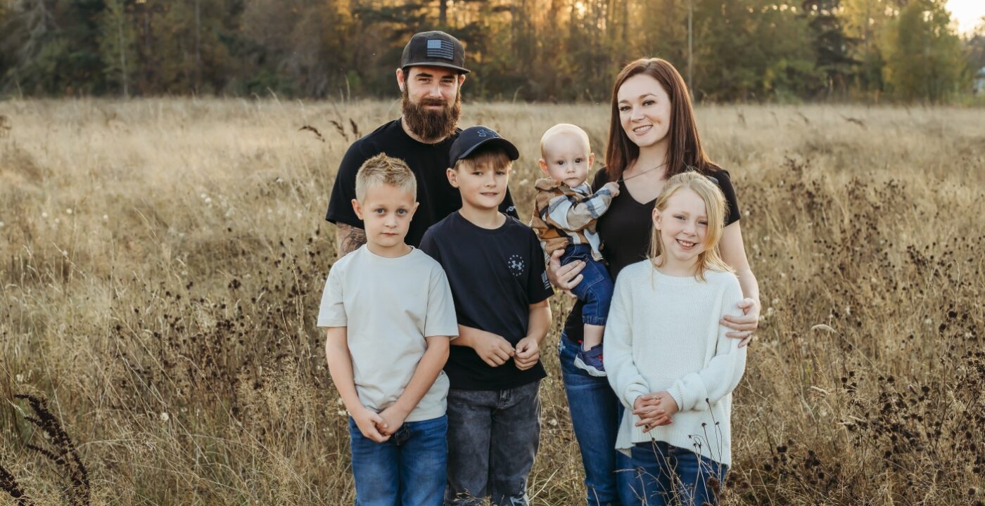 Family portrait of dad, mom, three boys and a girl in a field with tall grass