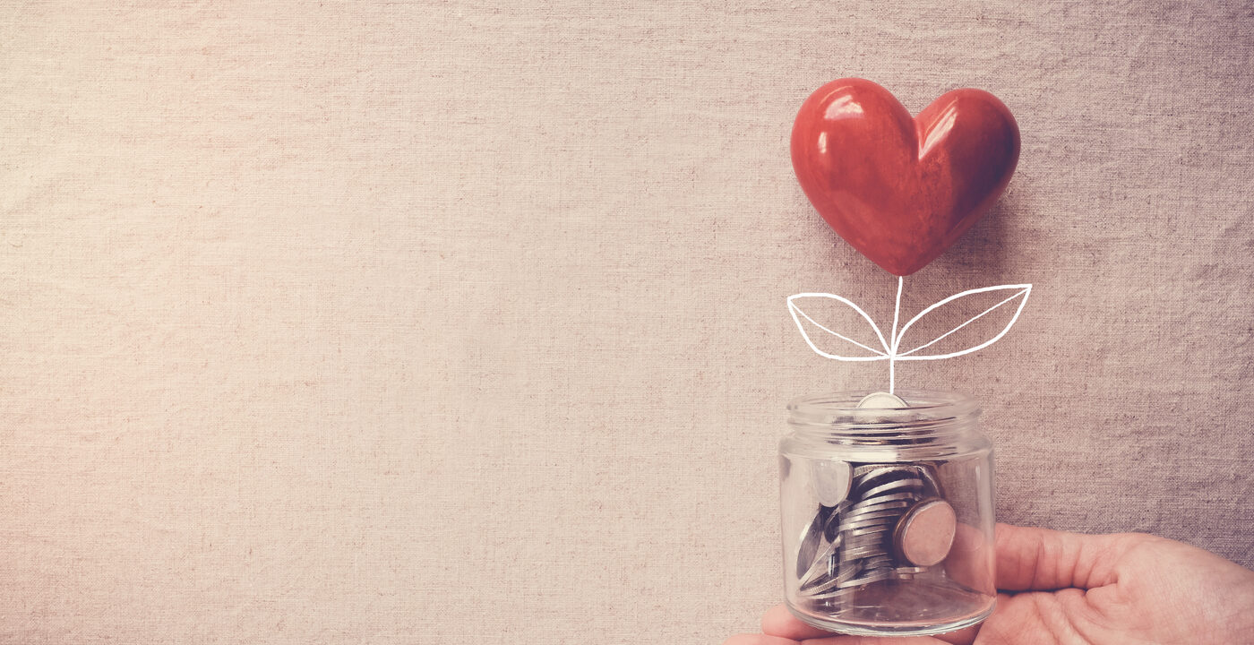White hand holds glass jar of coins with a glossy red heart appearing to “grow” out of the jar