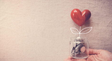 White hand holds glass jar of coins with a glossy red heart appearing to “grow” out of the jar