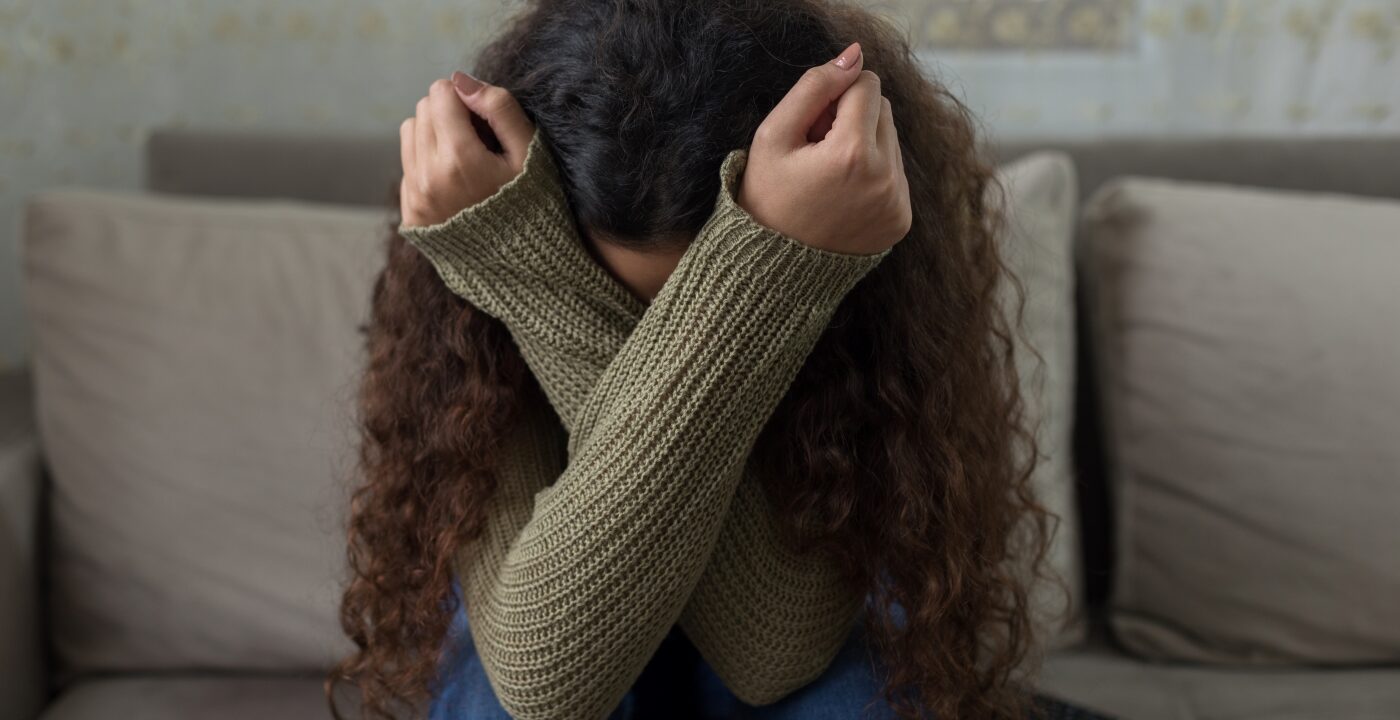 Woman visibly upset, covering face with arms while sitting on a couch