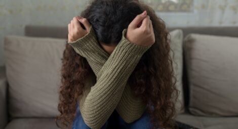 Woman visibly upset, covering face with arms while sitting on a couch