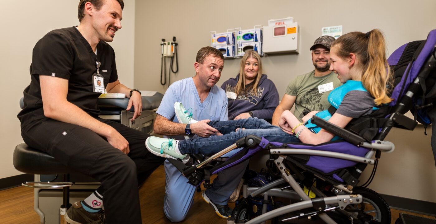 Two doctors speak with a patient in a power wheelchair while her parents sit nearby
