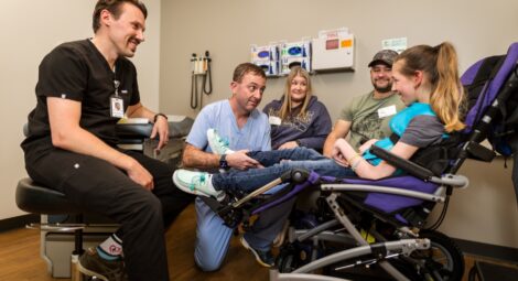 Two doctors speak with a patient in a power wheelchair while her parents sit nearby