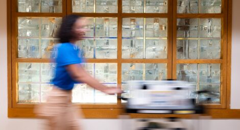 Woman in blue polo and khakis pushes a book cart down a hospital hallway