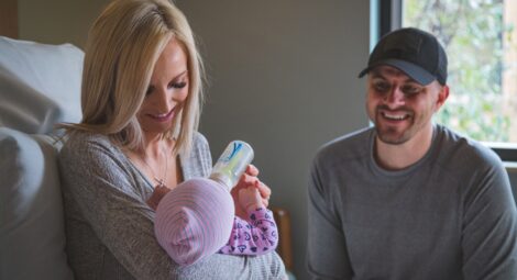Mother feeding baby with a bottle while smiling man looks on
