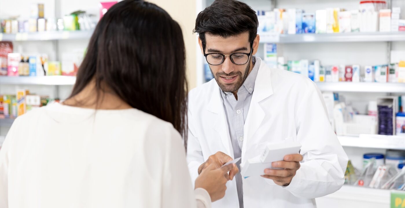 Male pharmacist reviews a prescription with an individual pictured from the back