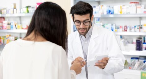 Male pharmacist reviews a prescription with an individual pictured from the back