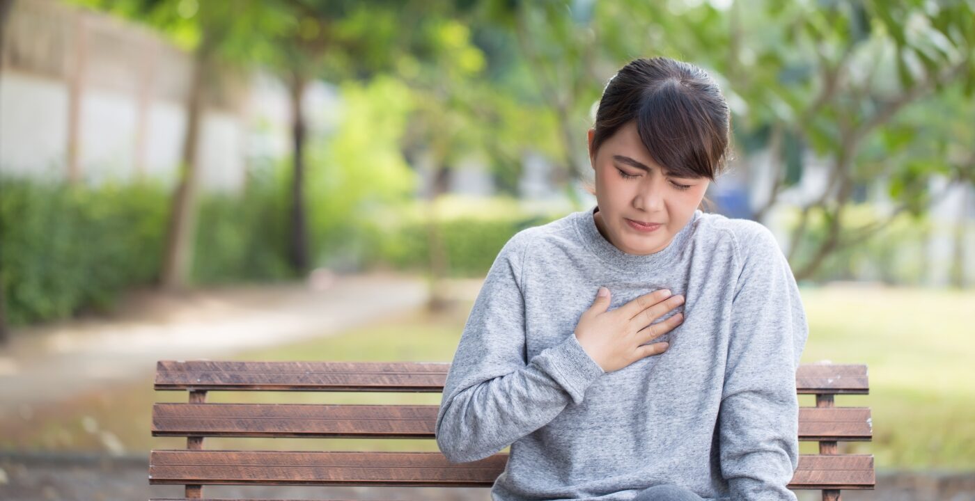 Woman sitting on park bench holding chest as if in pain