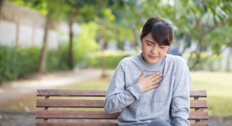 Woman sitting on park bench holding chest as if in pain