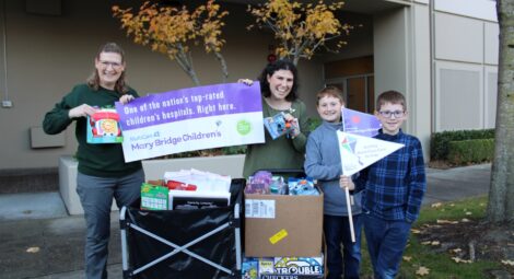 Two adults and two children post with boxes full of toys and purple and white Mary Bridge Children’s banners