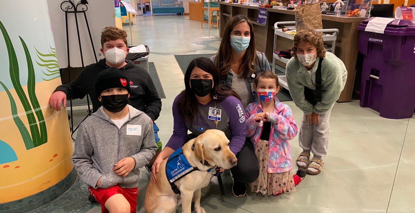 Group of children and adults, plus a golden retriever in a blue vest