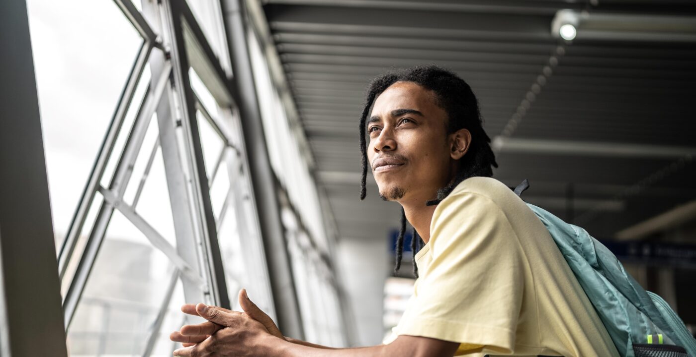Young adult male wearing a backpack gazing out a window