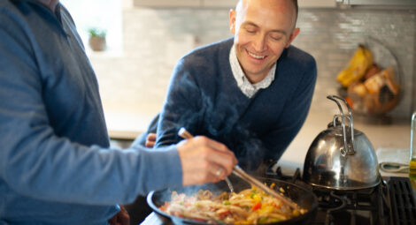 Two men stir a pan of food in a kitchen