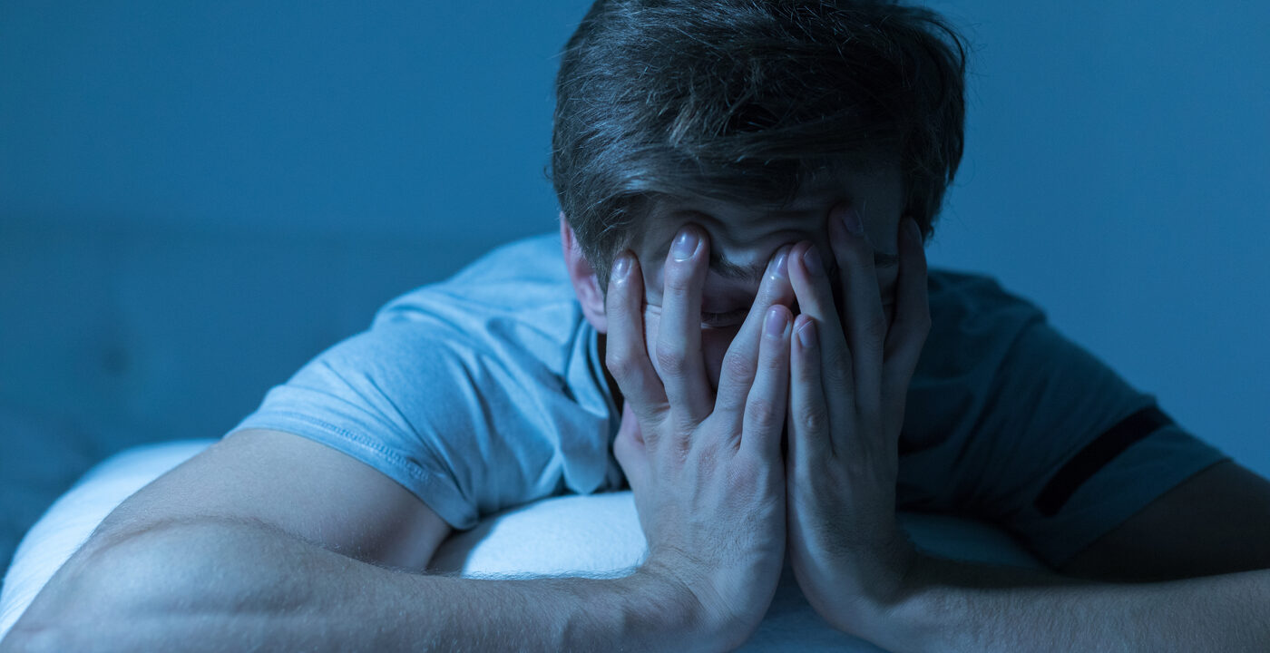 A man leaning on his pillow and covering his face with his hands
