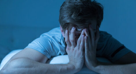 A man leaning on his pillow and covering his face with his hands
