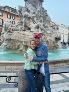 Man and woman embrace in front of fountain in Italy