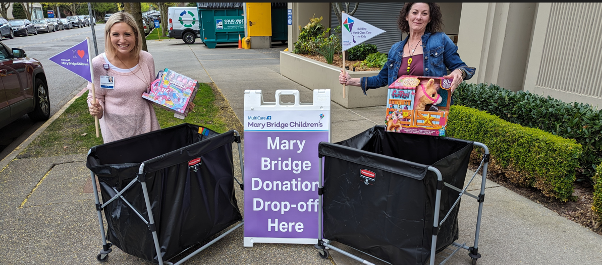Two of Lilly Reddy’s colleagues at MultiCare Auburn Medical Center smile in front a wagon full of new toy donations made in honor of Reddy’s late daughter.