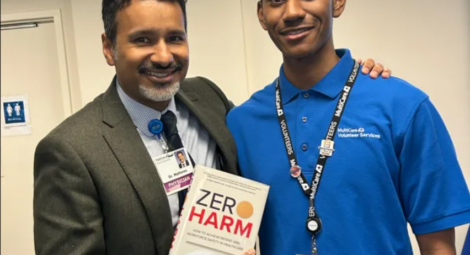 Man in suit holding “Zero Harm” book poses with young man in blue MultiCare Volunteer Services shirt