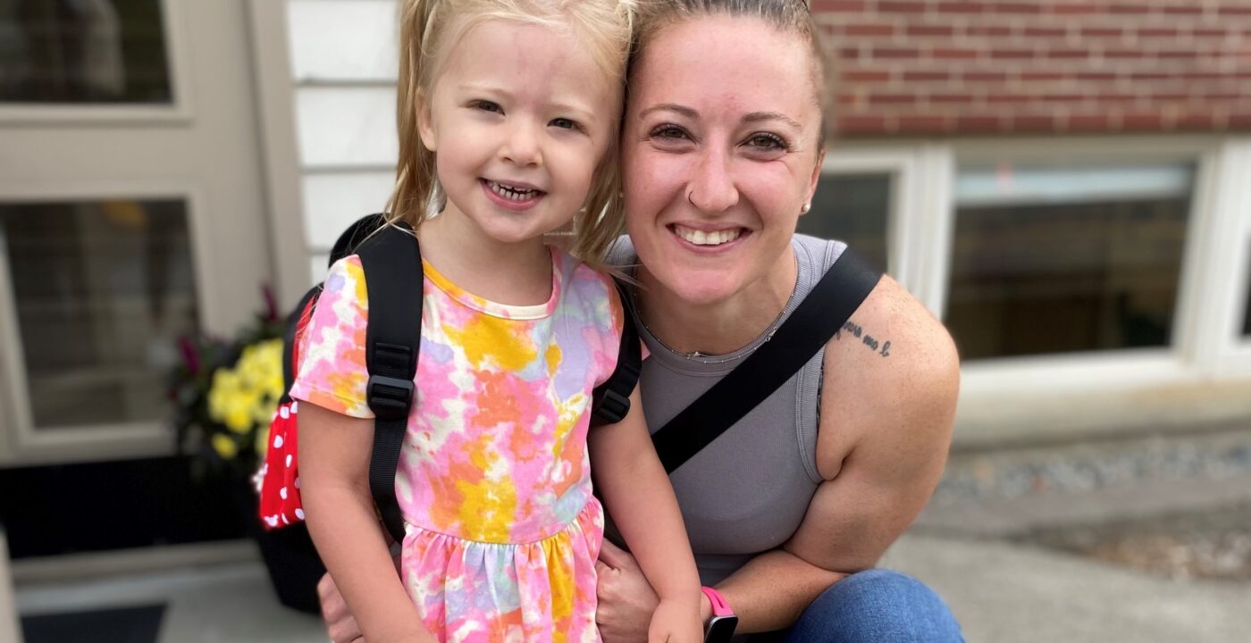 Woman in gray tank top and brown hair in a bun and a young blonde child in a dress