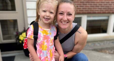 Woman in gray tank top and brown hair in a bun and a young blonde child in a dress
