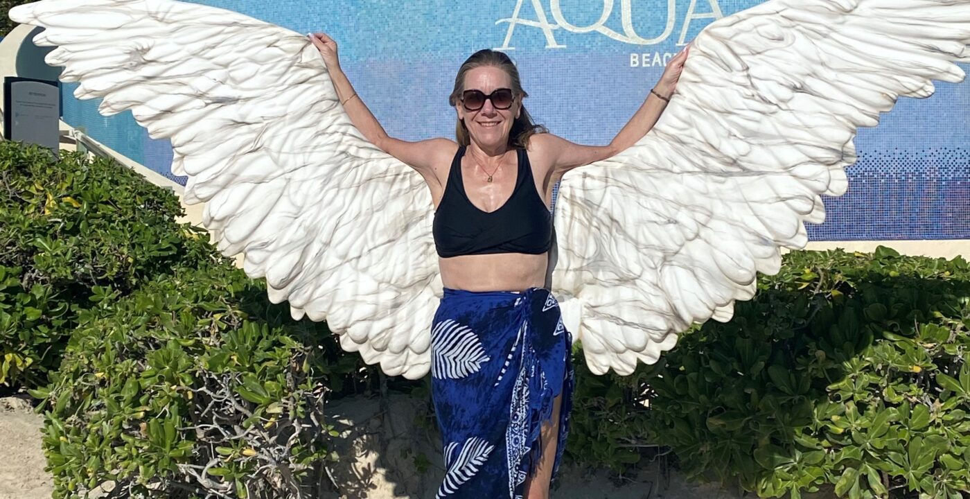 Woman on beach poses in front of statue of wings