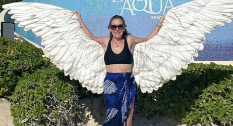 Woman on beach poses in front of statue of wings