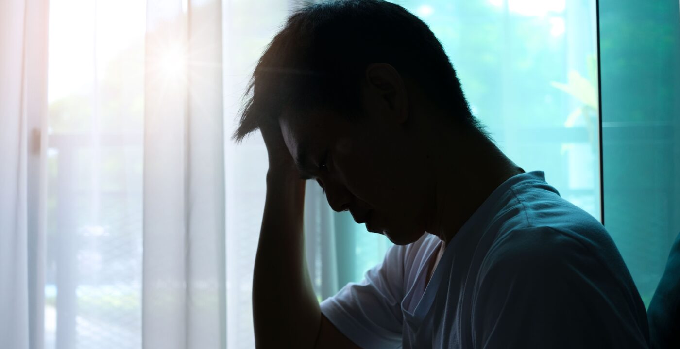 Man sitting in front of a window holding his head with his hand