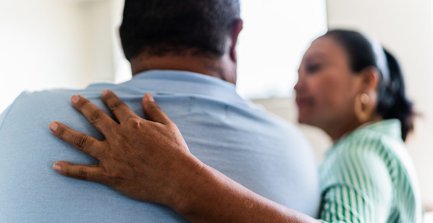 Woman puts a comforting arm around man’s shoulders