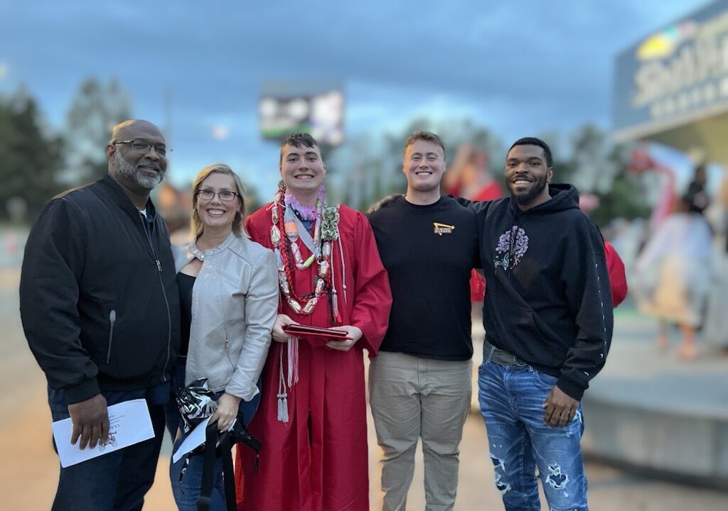 Group of smiling people, grad in red gown in middle, posing for a photo