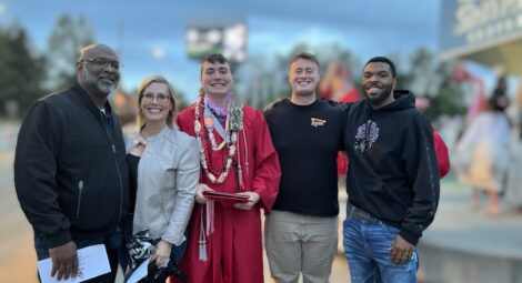 Group of smiling people, grad in red gown in middle, posing for a photo