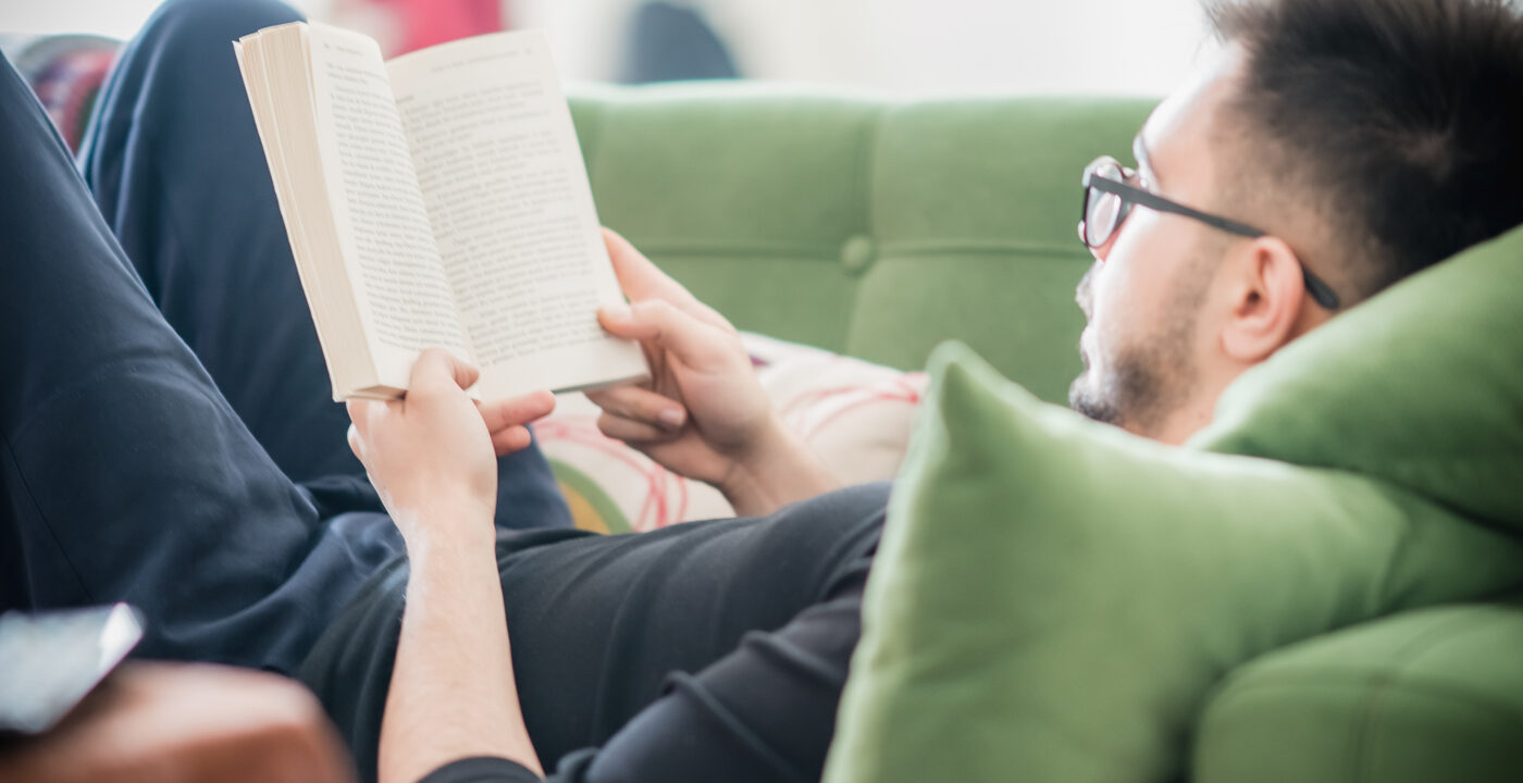Young man reading a book while lying on a green couch