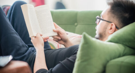 Young man reading a book while lying on a green couch