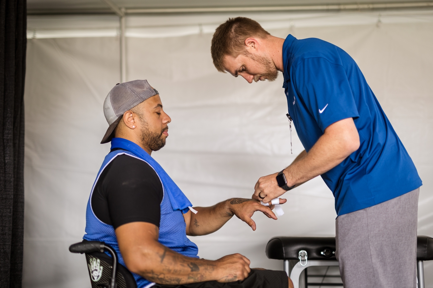 Man in blue T-shirt wraps finger of man sitting in a chair 