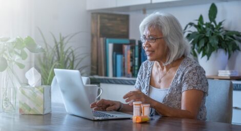 Senior woman sitting in front of a laptop next to medication bottles