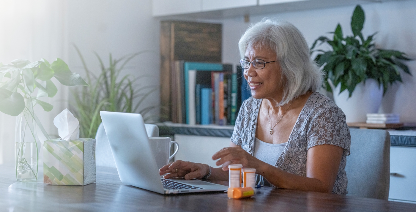 Senior woman sitting in front of a laptop next to medication bottles