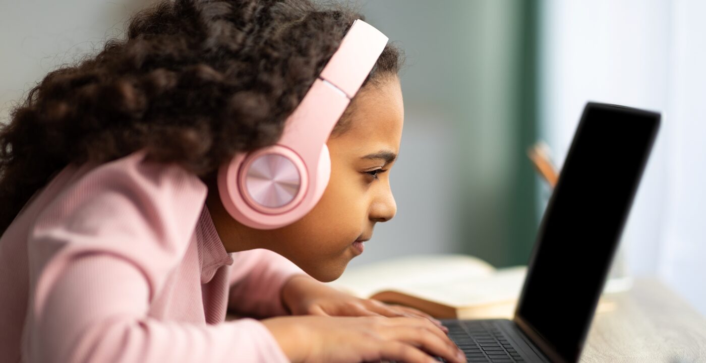 Young girl wearing headphones and squinting at a laptop