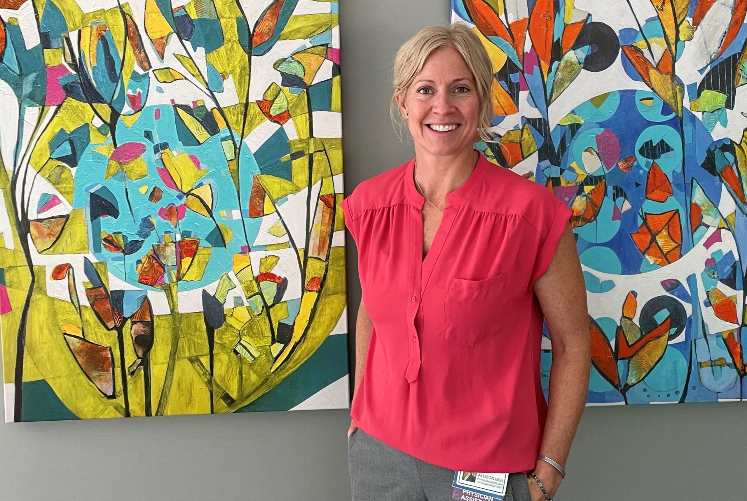 Woman in coral-colored top poses in front of two abstract paintings