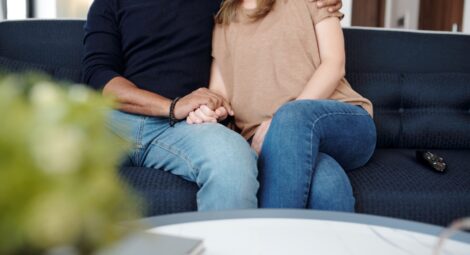 A man and a woman sitting on a blue couch holding hands
