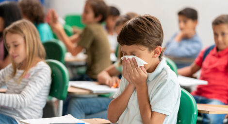 Child blowing nose sitting at classroom desk