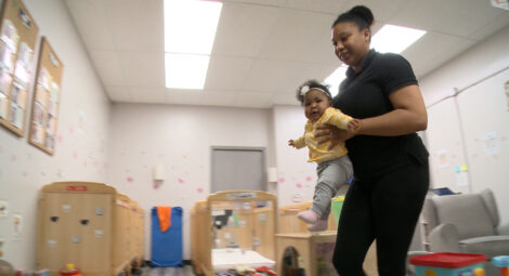 Woman carries baby across classroom